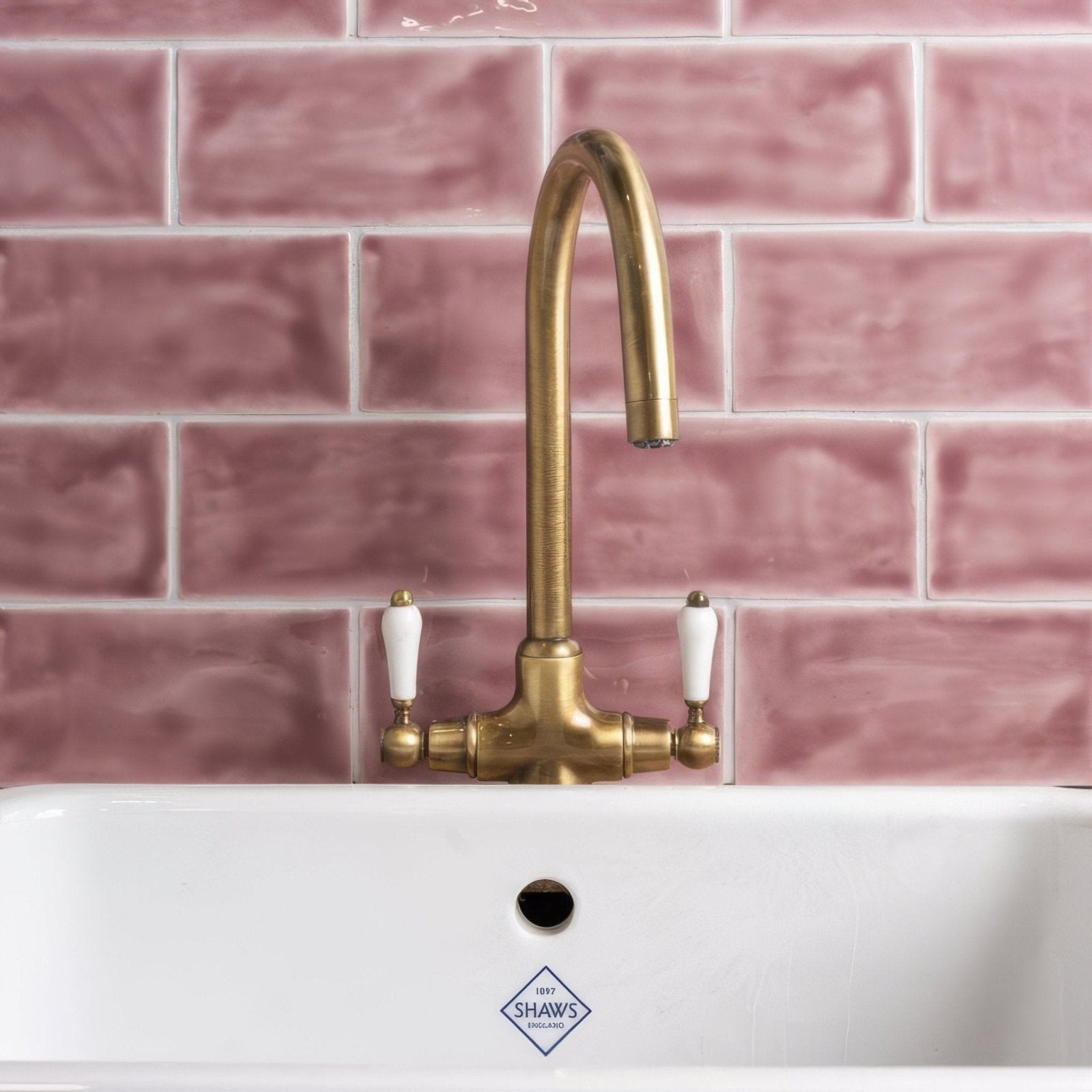 Brass faucet with white ceramic handles mounted on pink tayberry brick tile backsplash