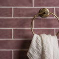 Gold-toned circular towel ring with sunburst-patterned backplate holding white waffle-weave towel in Tayberry large brick tile setting