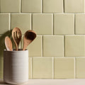 A white ceramic utensil holder with vertical ridges holding wooden spoons against a pale green thyme half tile backsplash