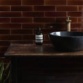 Dark amber glass bottle with black pump and minimalist white aesop label in tor brick tile design