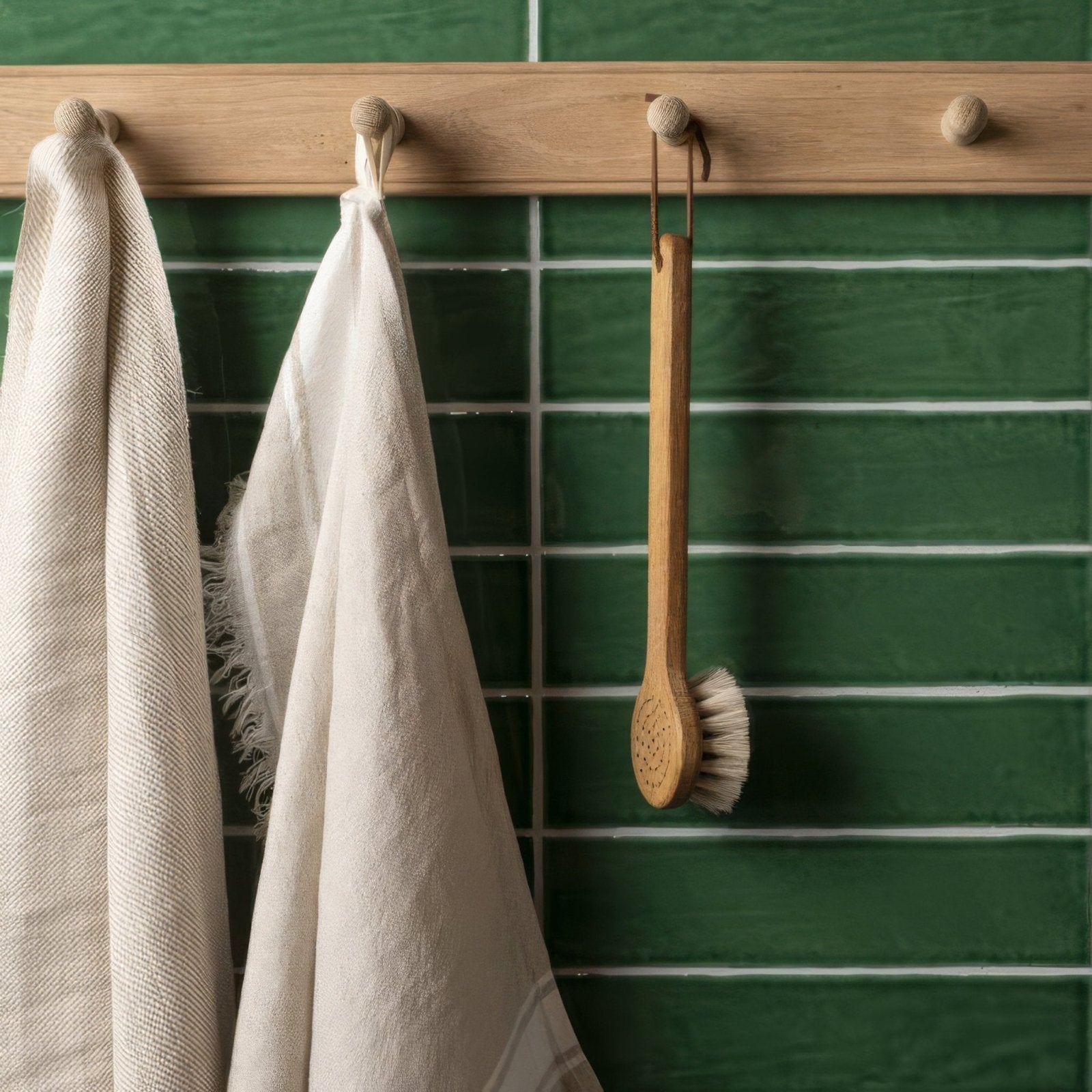 A wooden-handled bath brush with natural bristles hangs on a rustic wood rack next to tourmaline large brick tile