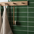 A wooden-handled scrub brush with natural bristles hanging on a tourmaline large brick tile wall-mounted rack