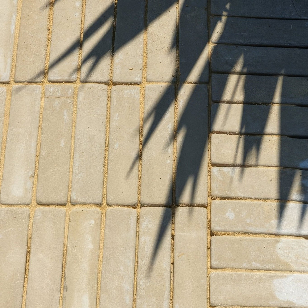 Beige rectangular trafalgar sandstone tumbled klinkers arranged in a herringbone pattern next to dark gray bricks