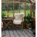 A cozy wooden chair draped with a fluffy off-white sheepskin throw on urban velasco patterned porcelain tile floor