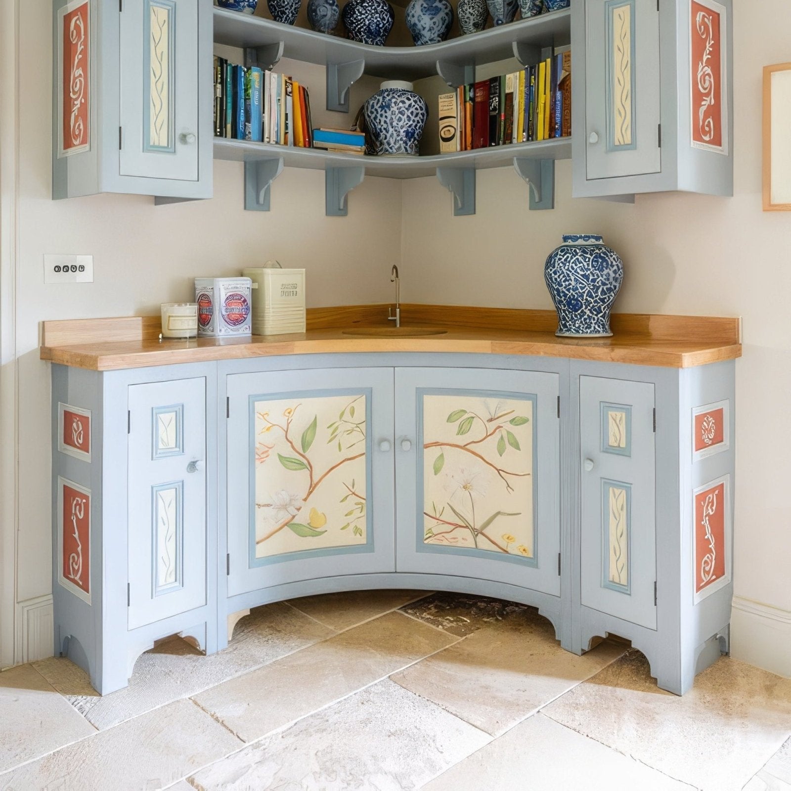 Light blue painted corner kitchen cabinet with decorative botanical panels and red-orange trim in vieux bourgogne limestone finish