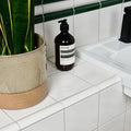 Aesop sleek dark amber glass bottle with black pump and white label placed on Victorian Style wall ceramic white square