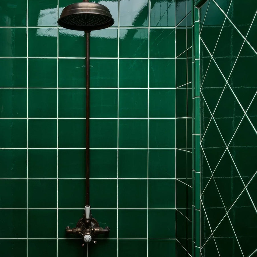 A dark bronze round showerhead with a long slender stem mounted on victorian style wall ceramic emerald green tiles