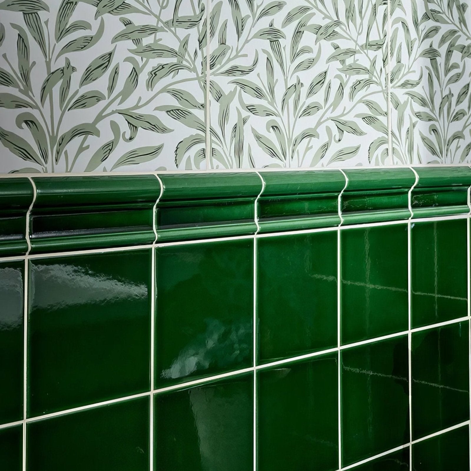 Deep emerald green ceramic tiles with glossy finish and white grout form a wall section topped by decorative molding