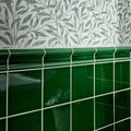 Deep emerald green ceramic tiles with glossy finish and white grout form a wall section topped by decorative molding
