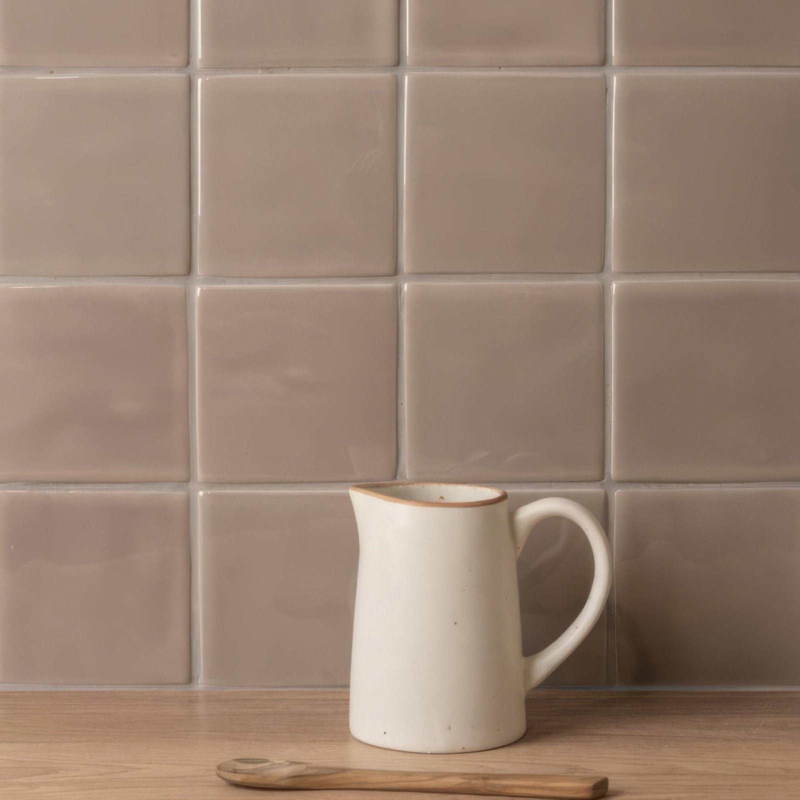 Cream-colored ceramic pitcher with rustic finish and subtle brown rim featured on walnut field tile background