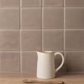 Cream-colored ceramic pitcher with rustic finish and subtle brown rim featured on walnut field tile background