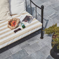 Beige and white striped outdoor cushion with black metal frame on wexford limestone cobble tumbled finish chair