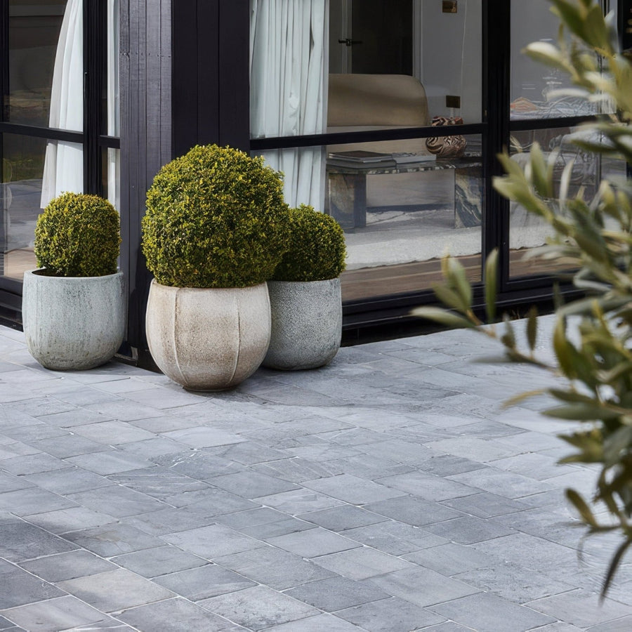 Three round green topiary bushes in textured gray wexford limestone cobble tumbled finish stone planters