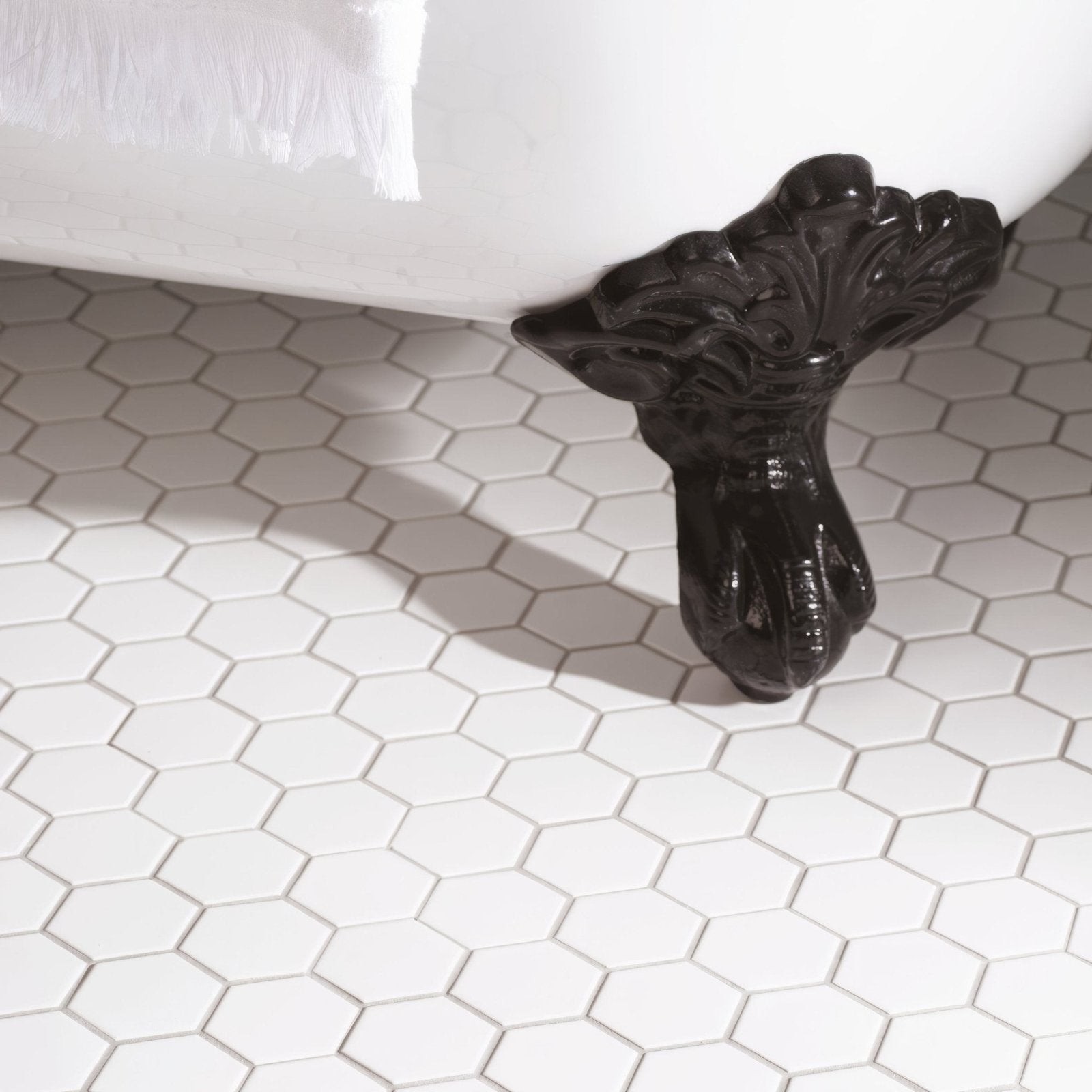 Black ornate claw foot supporting a white bathtub on a white large honeycomb floor mosaic tile surface