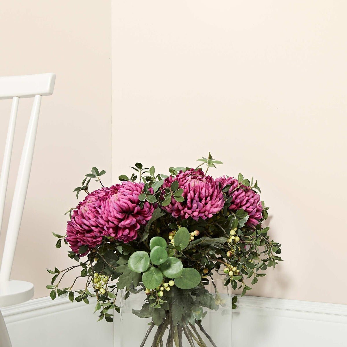 A white mulberry vase with a vibrant bouquet of deep magenta chrysanthemums green foliage and yellow berries