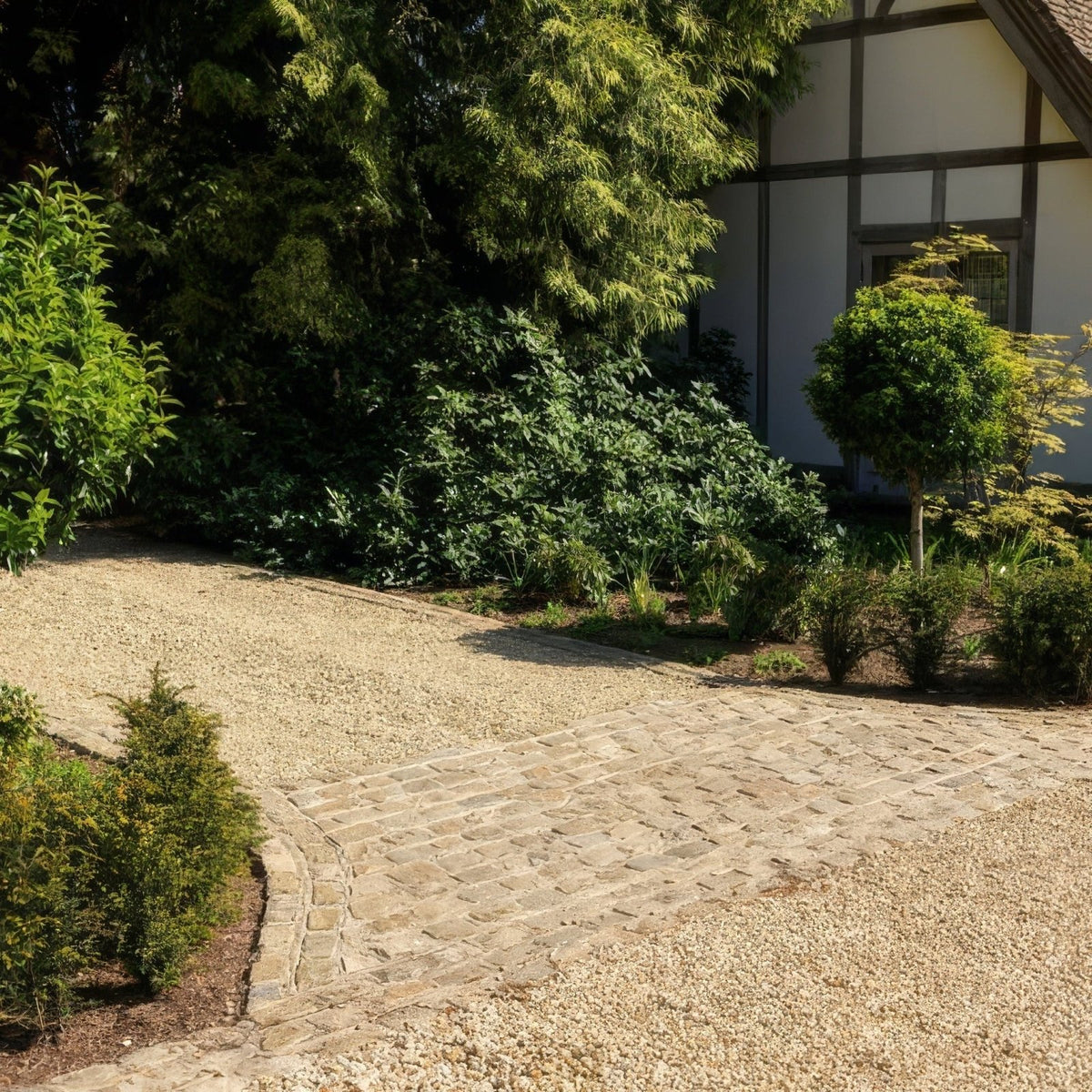 A curved stone pathway made of irregular light gray reclaimed and sawn windsor sandstone cobble bordered by gravel and shrubs
