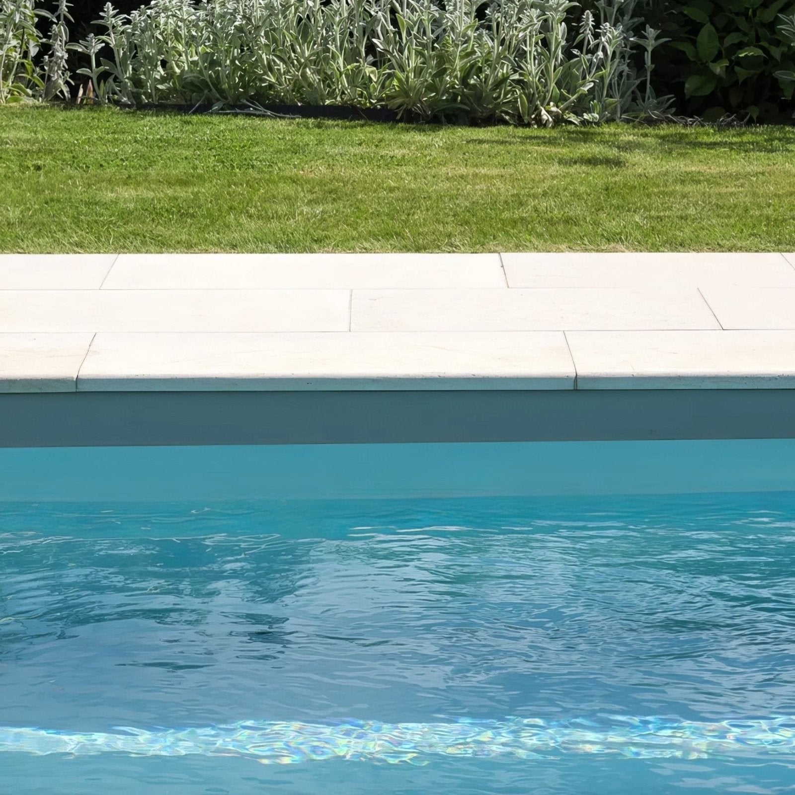 A sleek light gray wychwood limestone etched bullnose coping stone pool deck bordering clear blue water