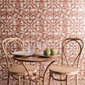 Rustic wooden table with round top and metal legs between two chairs against a patterned zayda mocha matt ceramic tile wall