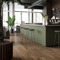 Canaiolo Castagno warm wood-effect flooring with an olive green bar counter and metal stools
