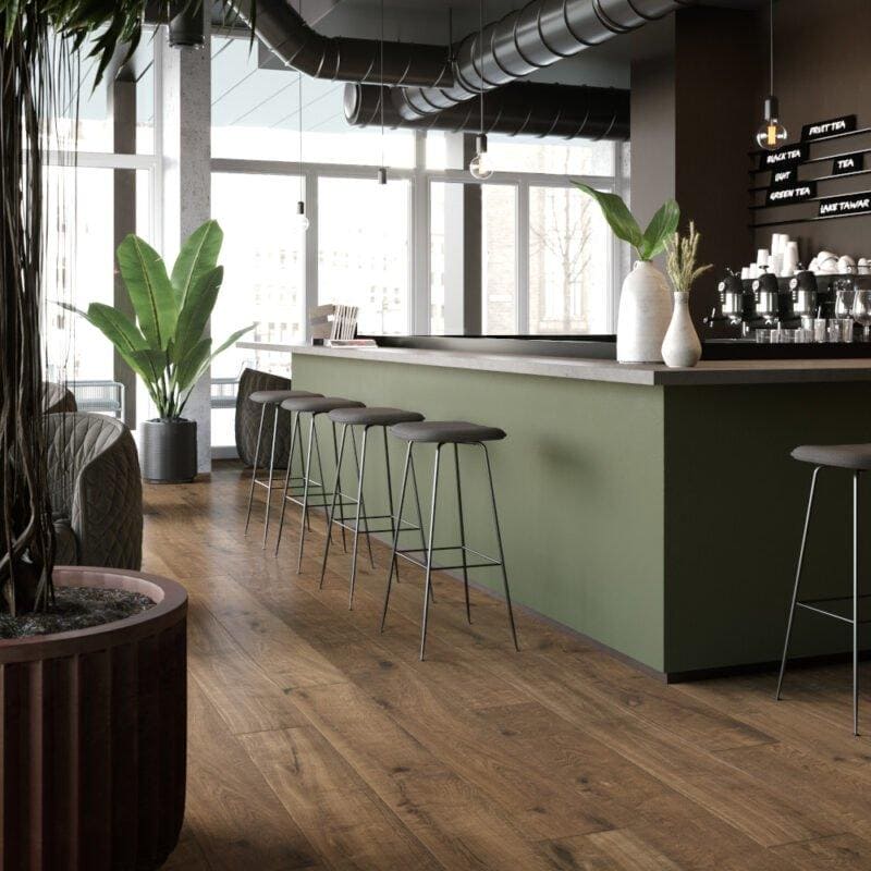 Canaiolo Castagno warm wood-effect flooring with an olive green bar counter and metal stools