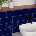 Deep blue glossy metro cobalto subway tiles with white grout lining a bathroom wall