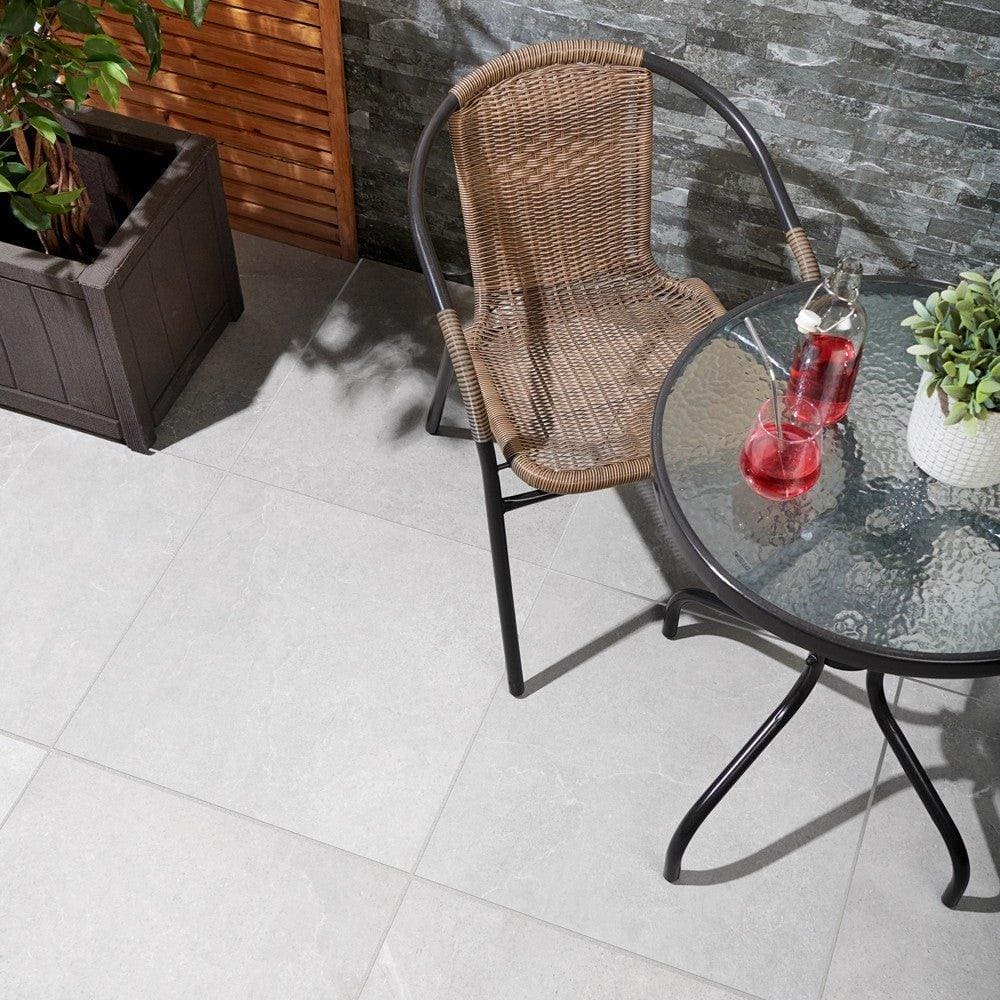 Pulse Grey Tiles grey stone-effect paving with a wicker chair