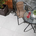 Pulse Grey Tiles grey stone-effect paving with a wicker chair
