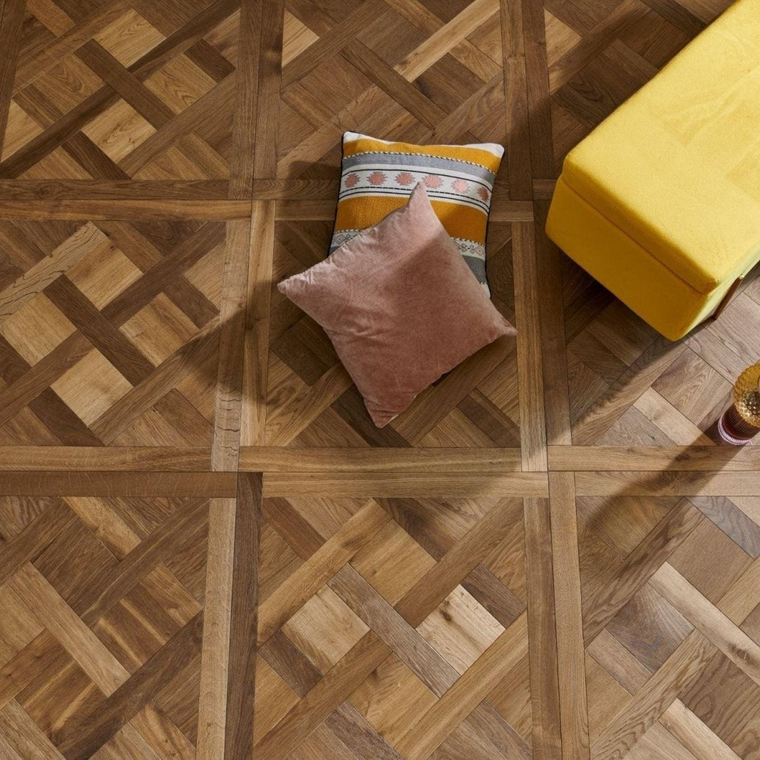 A soft pink velvet pillow resting on a patterned orange and gray cushion on a Sandringham Royal Oak parquet floor