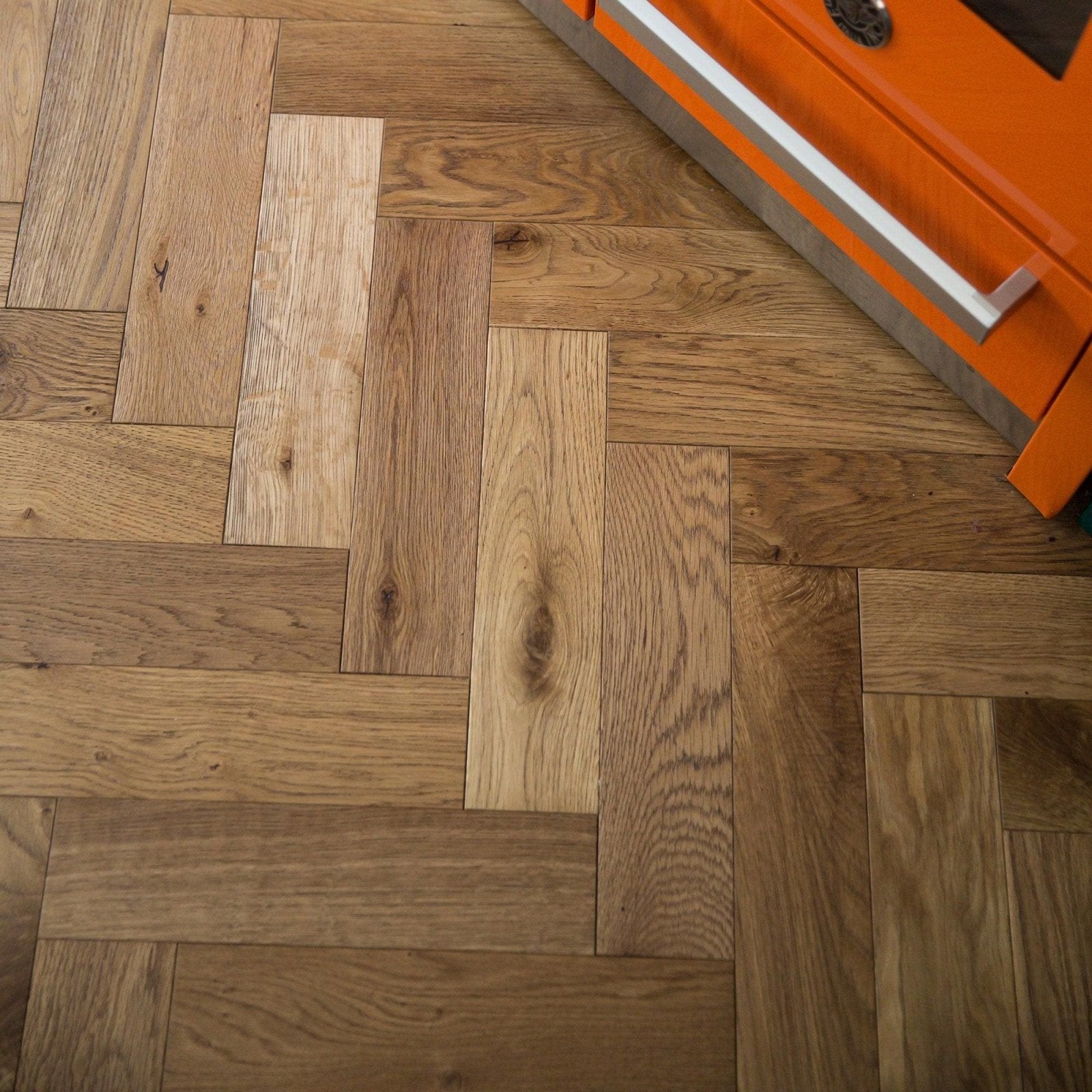 Herringbone-patterned smoked oak hardwood flooring with natural grain in varied light to medium brown tones